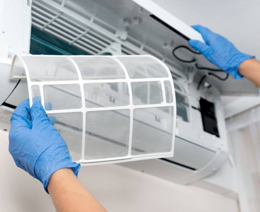 A person in blue gloves holds a window air conditioner, preparing to install it.